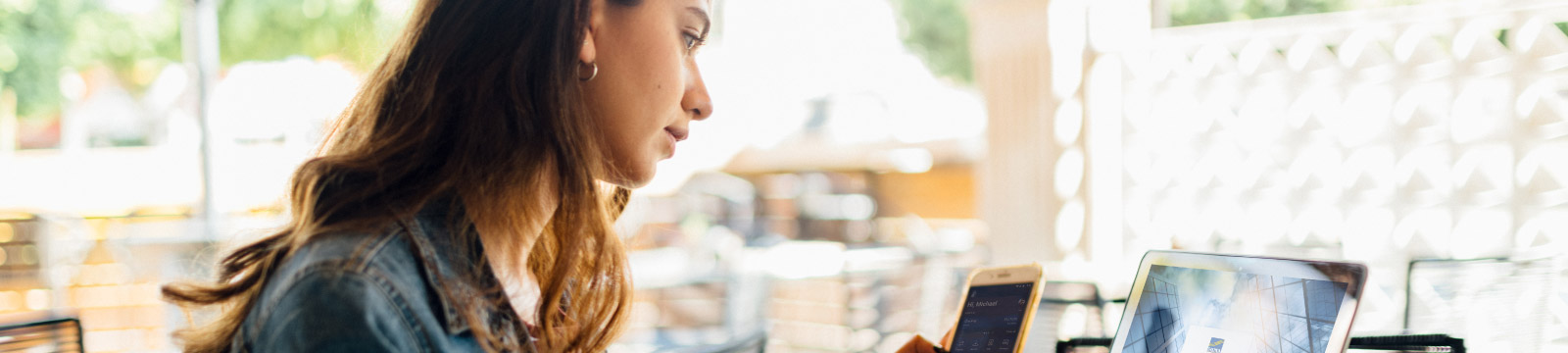 Woman looks at phone while sitting at her computer in a cafe.