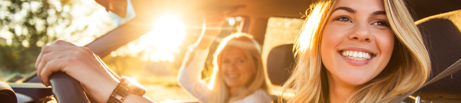 Happy daughter sits in a drivers seat with mother beside her.