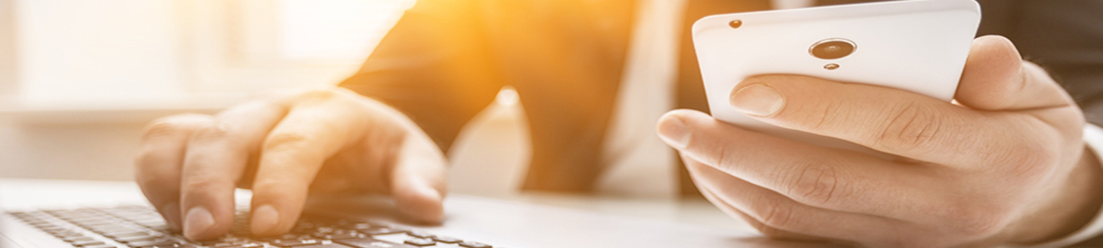 Person holding a smartphone in one hand and typing on a PC with the other hand.