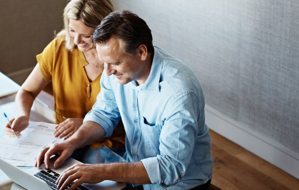 Happy middle aged couple site at table with paperwork and computer.