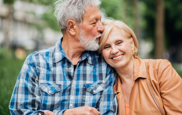 Mature couple site next to one another while man kisses woman's forehead.