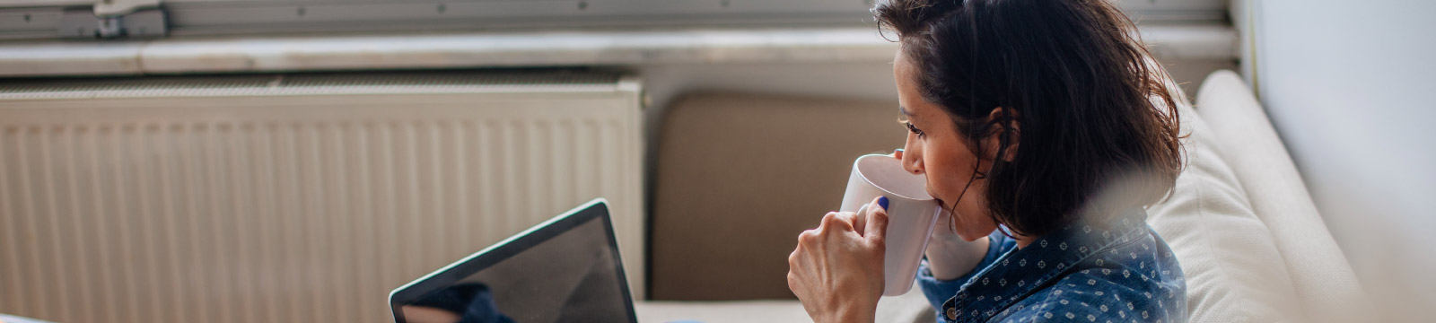 Woman sipping coffee while looking at computer in her home.